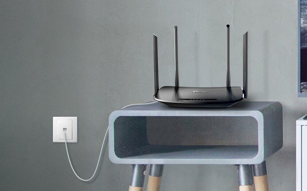 Router TP-LINK Archer VR300 Router umieszczony na szarej szafce, podłączony do gniazda telefonicznego w ścianie za pomocą białego kabla, modem, technologia