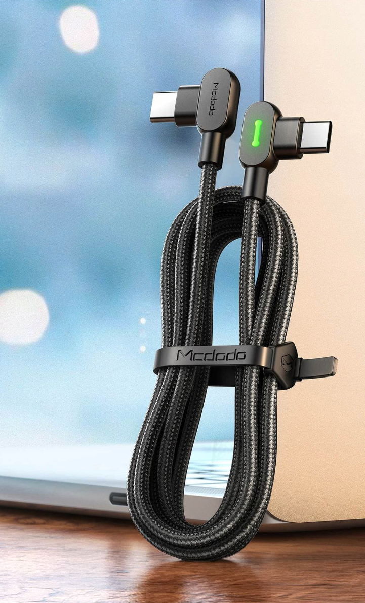 Czarny kabel USB-C z kątową wtyczką i zielonym wskaźnikiem LED, owinięty wokół laptopa. Na kablu widoczne jest logo \'Mcdodo\'.