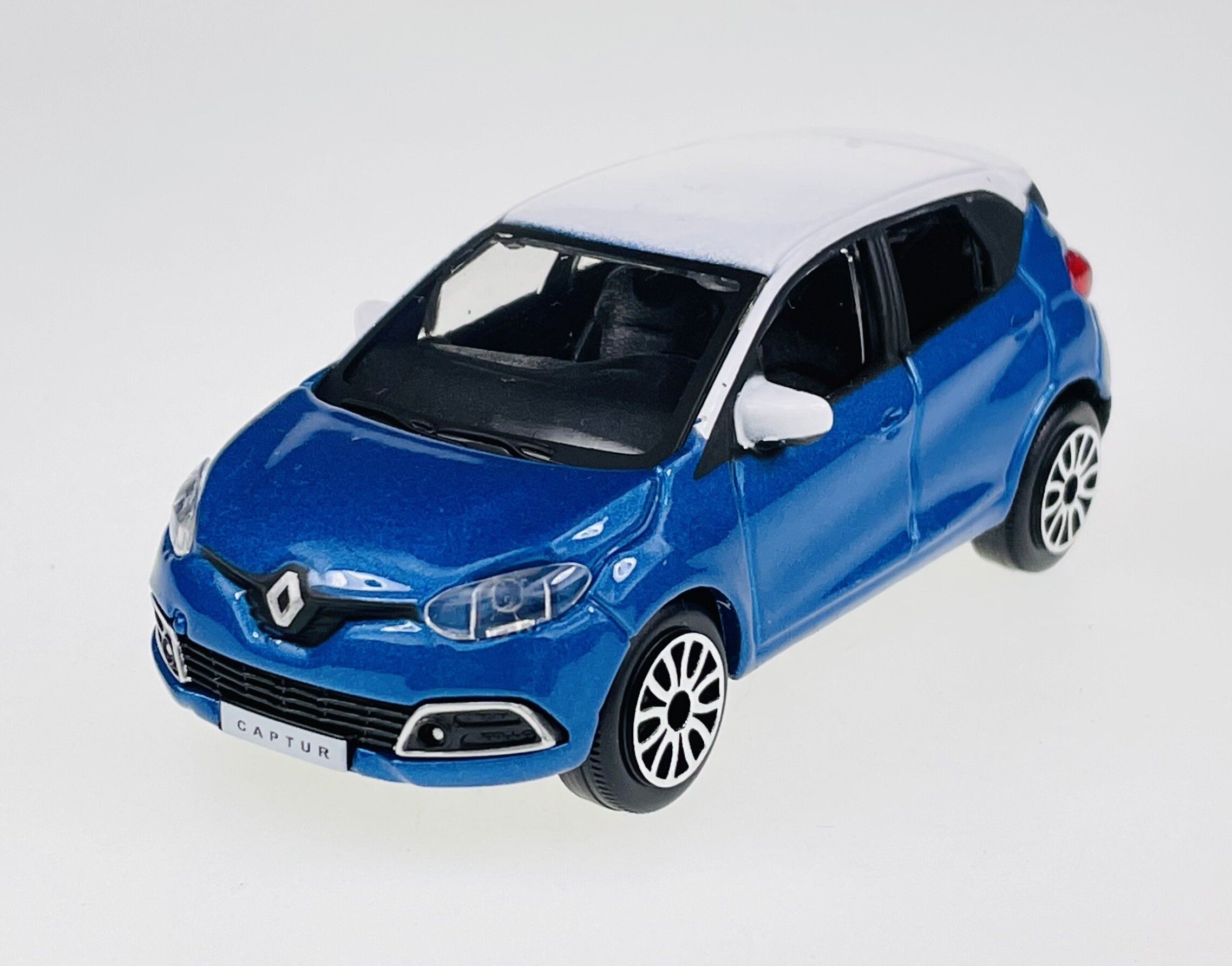 Model samochodu w kolorze niebieskim z białym dachem, z widocznym logo Renault na przodzie. Na tablicy rejestracyjnej widnieje napis \'CAPTUR\'.