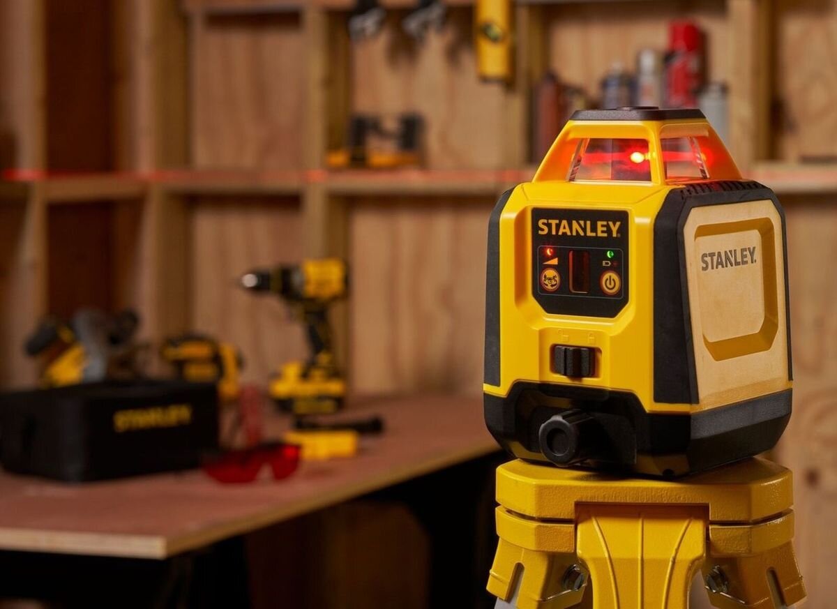 Laser rotacyjny STANLEY STHT77616-0, poziom, rotacja, zakres, szybkość, laser rotacyjny Stanley na statywie w warsztacie, widoczna czerwona linia.