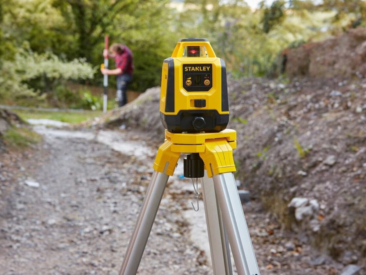 Laser rotacyjny STANLEY STHT77616-0, zasięg, zewnętrznie, ochrona, trwałość, Widok na niwelator Stanley na statywie podczas prac niwelacyjnych na zewnątrz.
