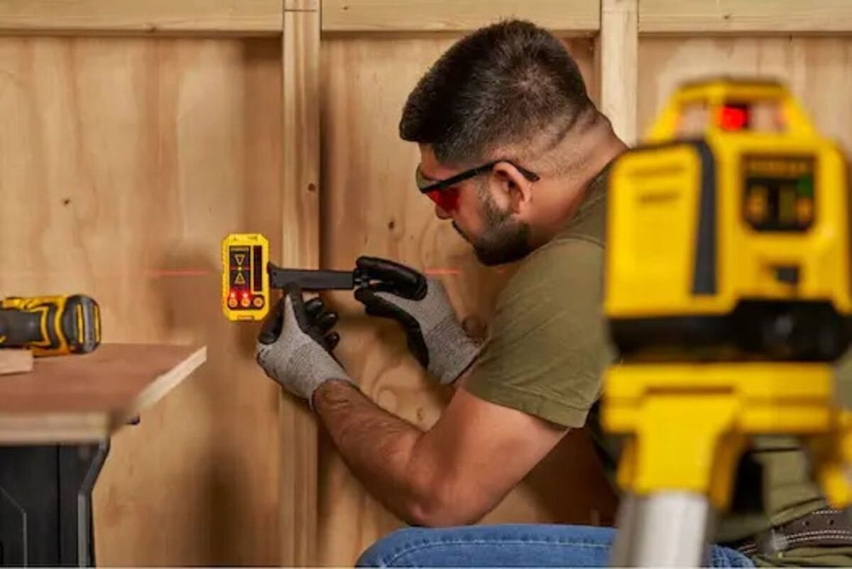 Laser rotacyjny STANLEY STHT77616-0, panel, ikony, diody, obsługa, Mężczyzna używa odbiornika laserowego Stanley przy drewnianej konstrukcji.