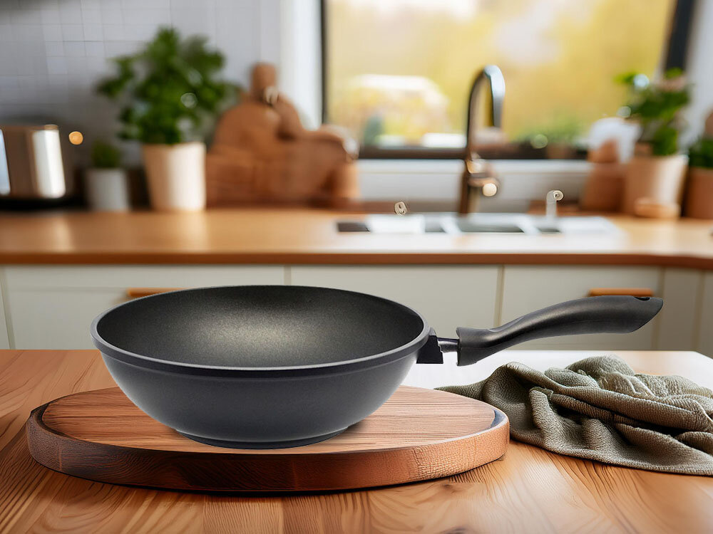 Patelnia wok ELO Alucast 9151826 28 cm patelnia znajduje się na desce czarna patelnia lezy bokiem czarny uchwyt kuchenne tło elegancki design staranne solidne wykonanie kulinarne eksperymenty specjalnie zaprojektowana powłoka Wygodny, żaroodporny uchwyt komfortowe i bezpieczne gotowanie 