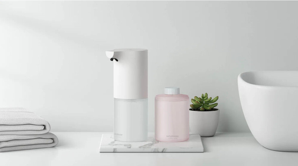 DOZOWNIK DO MYDŁA XIAOMI MI AUTOMATIC FOAMING SOAP DISPENSER 29349 BIAŁY Zdjęcie ukazuje elegancki, bezdotykowy dozownik mydła w piance stojący na marmurowej podstawce obok różowego pojemnika z zapasem. Jasne tło z ręcznikami, białą umywalką i małą rośliną tworzy nowoczesną, minimalistyczną aranżację łazienki