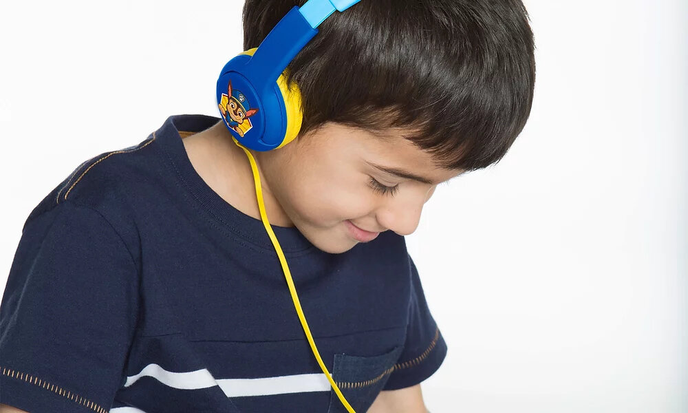 Dziecko nosi niebiesko-żółte słuchawki z motywem Psi Patrol. Słuchawki mają żółty kabel i widoczne logo postaci z bajki.