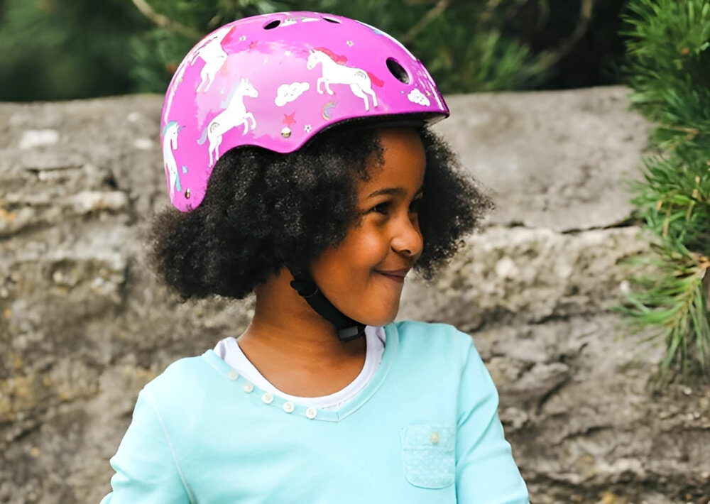 Kask HORNIT Unicorn Fioletowy dla Dzieci (rozmiar S) dziecko w kasku patrzy w bok w tle betonowe ogrodzenie drzewa bezpieczeństwo wygoda aktywność