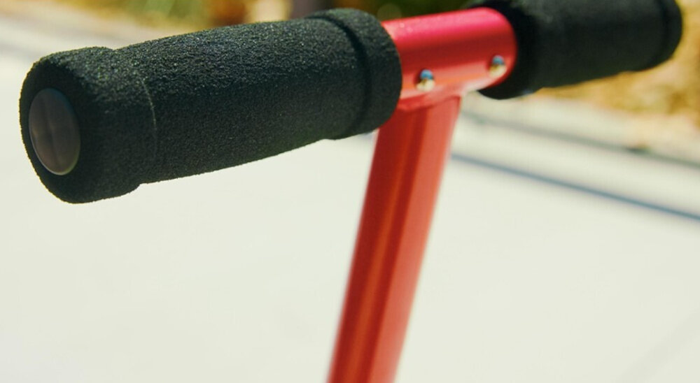 Hulajnoga RAZOR Sport S Czerwony zbliżenie na uchwyty kierownicy stalowa kierownica o wysokości 83 cm piankowe rączki chronią dłonie przed otarciami pewny chwyt bezpieczną pozycję podczas jazdy możliwość złożenia rączek
