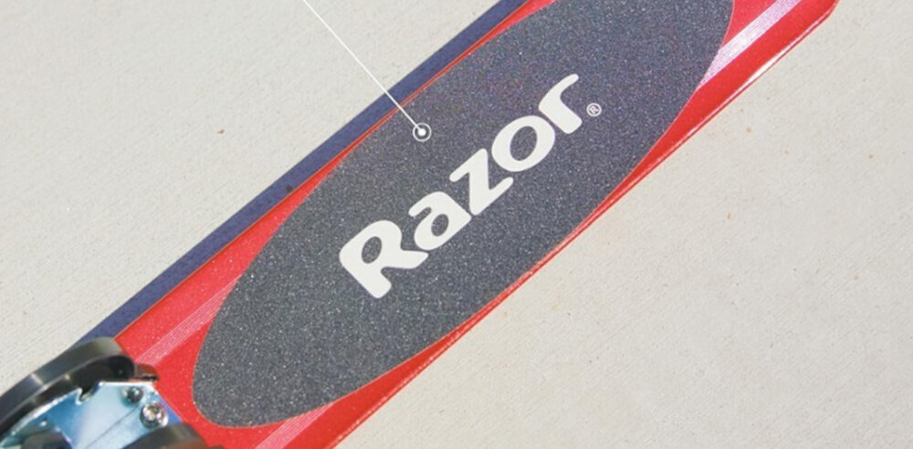 Hulajnoga RAZOR Sport S Czerwony zbliżenie na platformę na tle ulicy lekka platforma z wysokiej jakości aluminium antypoślizgowa powierzchnia szeroki podest o wymiarach 44 x 9,2 cm bezpieczne użytkowanie makymalna waga użytkowanika do 100 kg solidność komfort