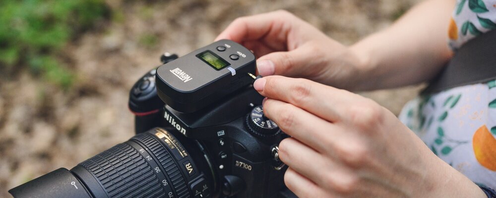 Osoba trzyma aparat fotograficzny z zamontowanym urządzeniem z logo \'Newell\'. Aparat ma widoczny obiektyw i oznaczenie \'Nikon\'.