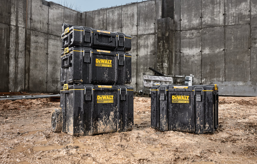 Skrzynka narzędziowa DEWALT DWST83342-1 plac budowy piasek skrzynia ustawiona na piasku obok 3 inne skrzynie ustawione jedna na drugiej należy do systemu ToughSystem 2.0 Toolbox w pełni kompatybilna z produktami ToughSystem pierwszej generacji można łączyć nowe elementy z już posiadanymi modułami dowolnie rozbudowywać zestaw