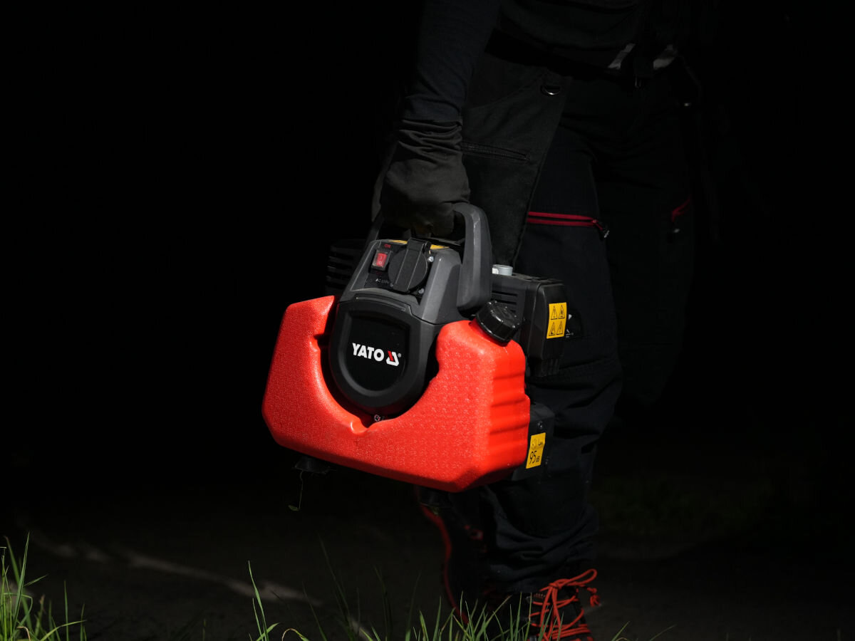 Agregat prądotwórczy YATO YT-85481, prąd, zasilanie, moc, energia, w porze nocnej osoba przenosi agregat w jednej ręce