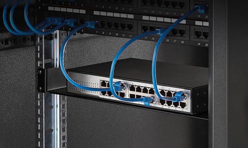 Półka EXTRALINK EX.12745 Urządzenie sieciowe z podłączonymi niebieskimi kablami ethernet leży na czarnej metalowej półce zamontowanej wewnątrz szafy rack