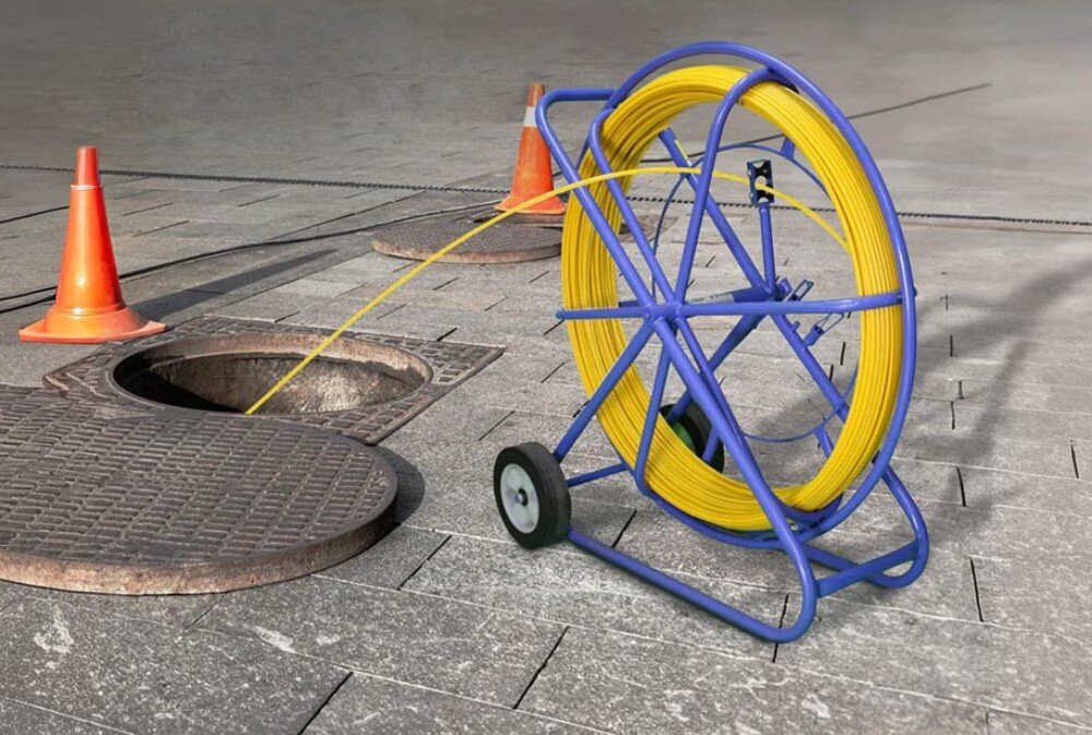 Pilot do przeciągania kabli EXTRALINK EX.13902 Niebieski stojak z żółtym przewodem ustawiony na ulicy z przewodem wchodzącym do studzienki kanalizacyjnej