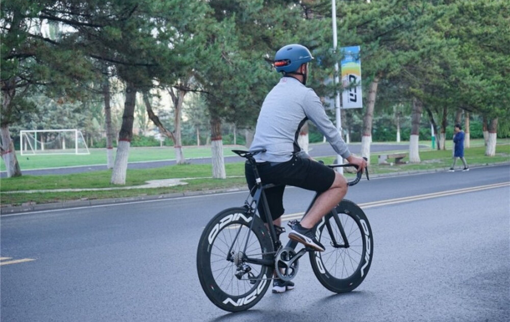 Kask LIVALL C20 Niebieski (rozmiar M) miasto droga osoba w kasku widoczna z boku jedzie po ulicy w tle drzewa funkcja automatycznego uśpienia i wzbudzenia oszczędzać energię system sam reaguje na brak aktywności wydłużając czas pracy klasa szczelności IPX4 chroni elektronikę przed zachlapaniem wodą