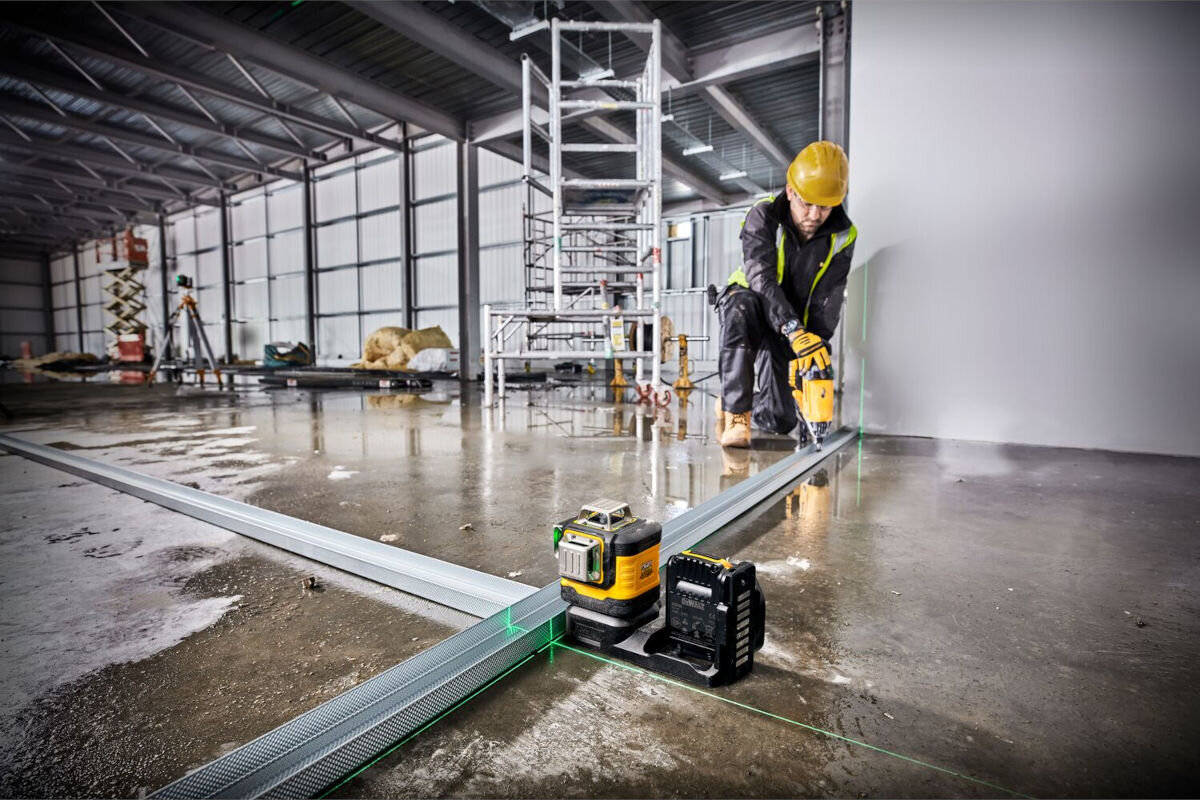 Laser DEWALT DCE089D1G18, mierzenie, laser, pomiar, budowa, mężczyzna pracuje przy listwie na placu budowy, obok laser na ziemi