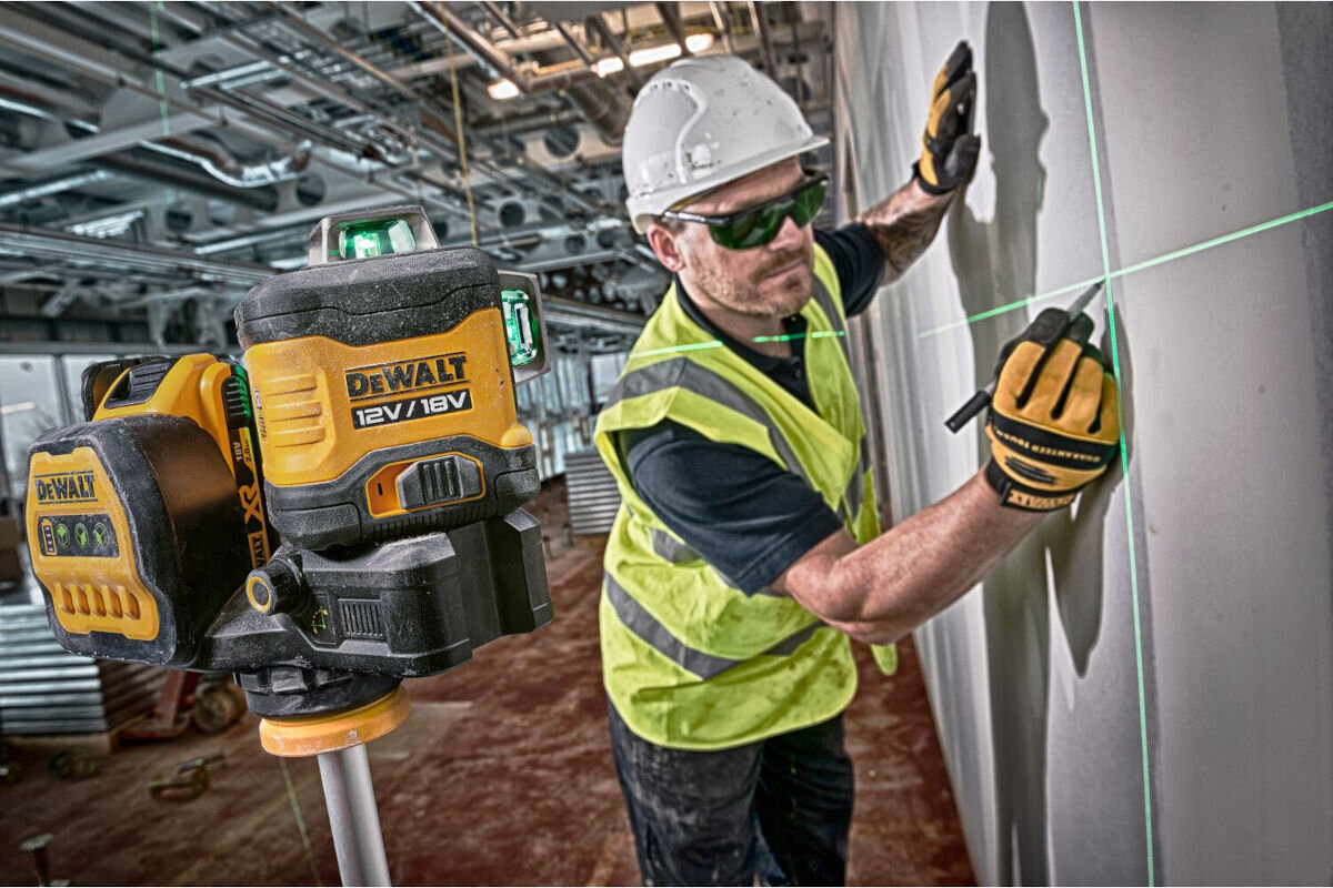 Laser DEWALT DCE089D1G18, gwinty, statywy, wbudowany, uchwyt, magnetyczny, mężczyzna odmierza na ścianie trasy lasera, obok laser na stojaku