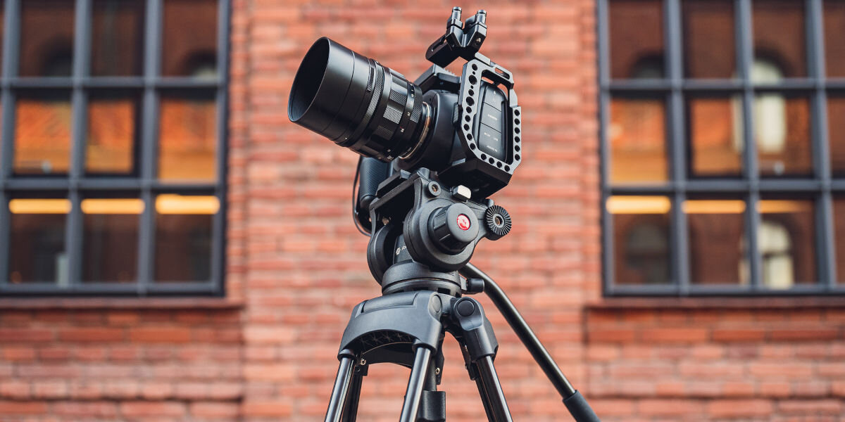 Statyw FOTOPRO DV-2, stojak, kamerowanie, nagrywanie, stabilne, statyw z zamontowanym aparatem frontem prawo skos w tle ceglany budynek