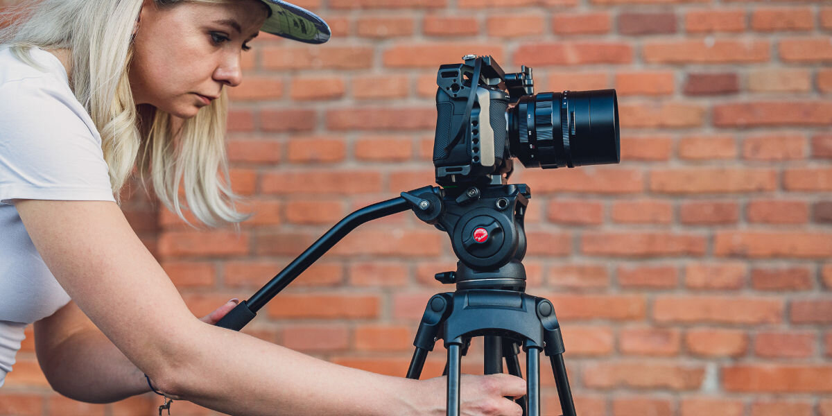 Statyw FOTOPRO DV-2, niezależne, osie, panoramowanie, pochył, kobieta ustawia statyw z rękojeścią i aparatem na nim, w tle ceglana ściana