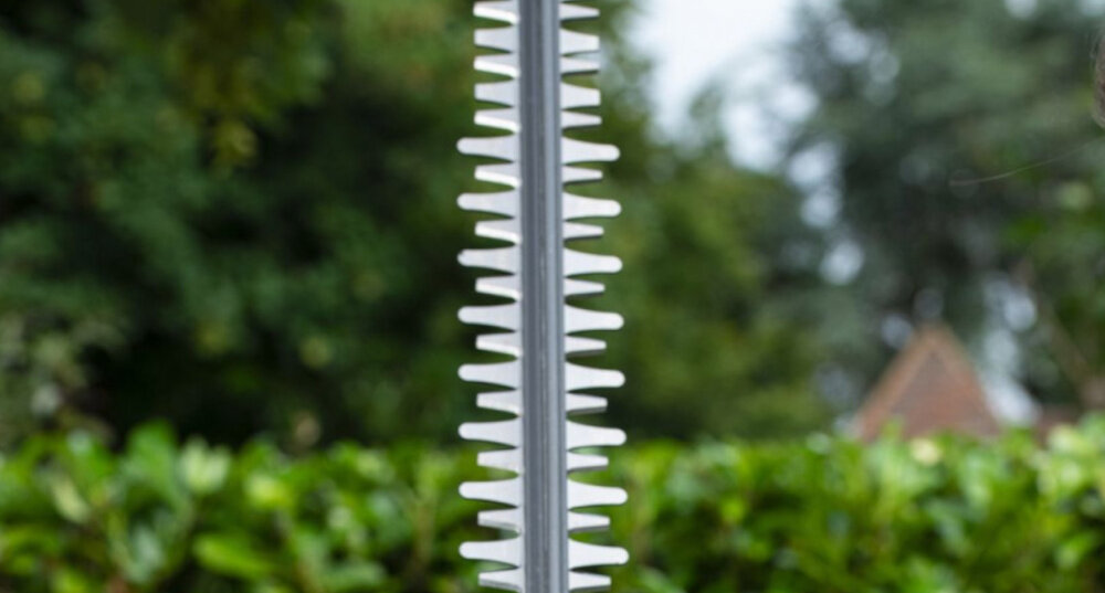 Nożyce do żywopłotu RYOBI RY18HT55A-0 akumulatorowe ogród zbliżenie na ostrza w tle żywopłot dom drzewa szlifowane diamentowo faliste ostrza ogranicza strzępienie gałęzi wysoka prędkość pracy 1350 obr./min