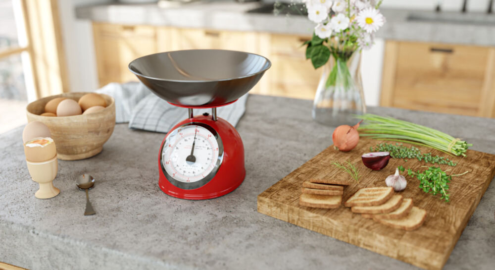 Waga kuchenna ETA Storio 577790030 precyzyjne ważenie czerwona waga stoi na blacie srebrna miska duży wskaźnik obok składniki na desce  