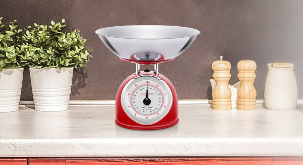 Waga kuchenna ETA Storio 577790030 czerwona waga duży wskaźnik srebrna misa obok stoją przyprawniki  do ważenia składników aż do 5 kg precyzja do 25 g funkcja zmiany jednostek gramy kilogramy funty uncje funkcjonalność kreatywność dokładność 