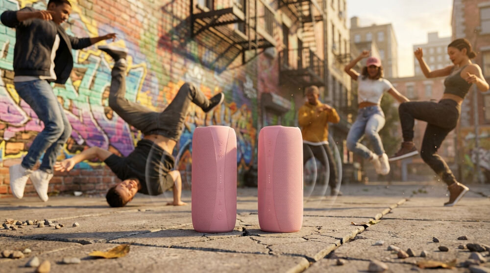 Dwa pionowo ustawione głośniki Bluetooth XMUSIC na miejskiej ulicy, otoczone przez grupę tancerzy wykonujących akrobacje na tle ceglanych budynków i graffiti.