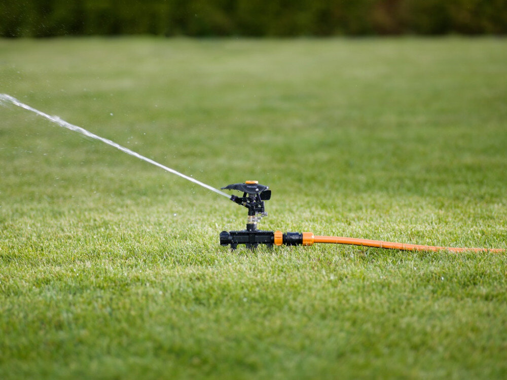 Zraszacz FISKARS 1023656, zraszacz, ogród, kółka, mobilność, zraszacz podlewa trawnik w ogrodzie w słoneczny dzień