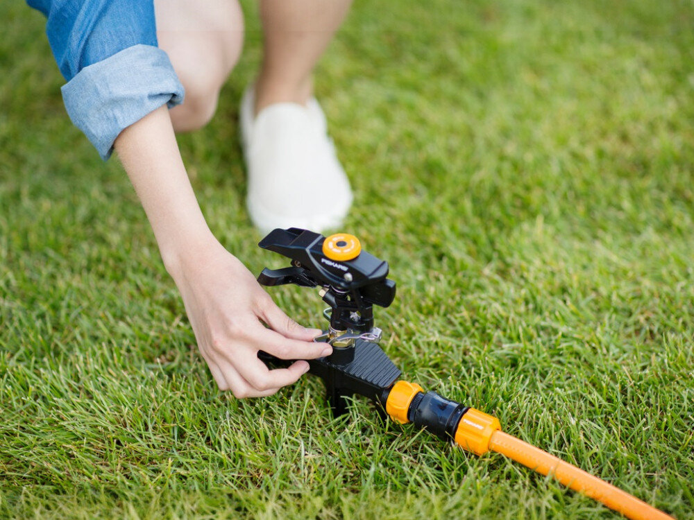 Zraszacz FISKARS 1023656, strumień, deszcz, mgiełka, rośliny, osoba reguluje pokrętło zraszacza