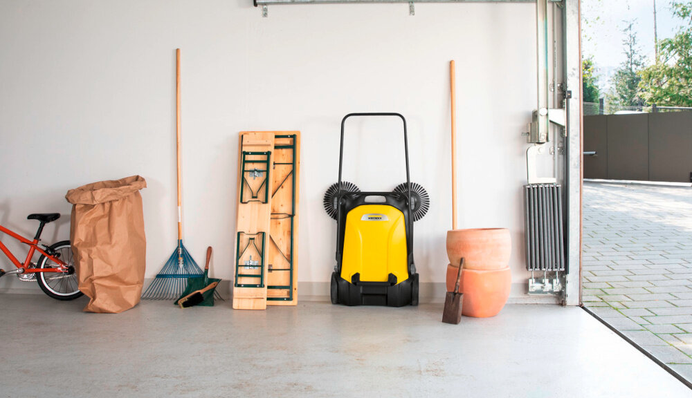 Zamiatarka ręczna KARCHER S4 Twin 2-in-1 1.766-365.0 garaż złożona zamiatarka oparta o ścianę w garażu obok inne narzędzia w tle podjazd i płot porządek sprzątanie wszechstronne zastosowanie