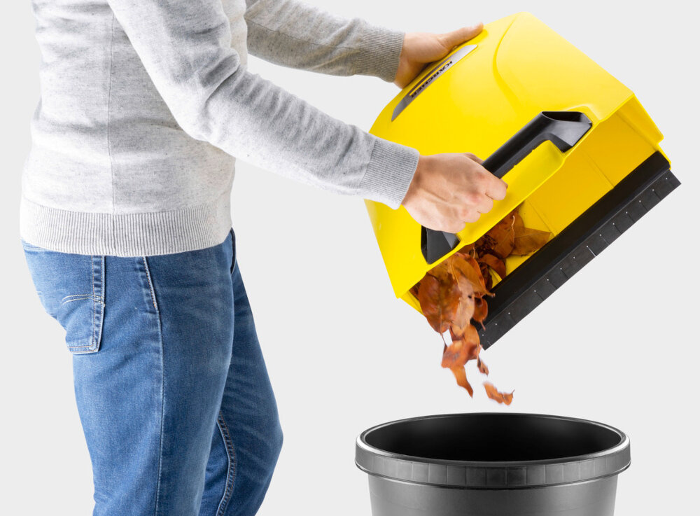 Zamiatarka ręczna KARCHER S4 Twin 2-in-1 1.766-365.0 jasne tło osoba wysypuje liście ze zbiornika do kubła na śmieci zintegrowany zbiornik na zanieczyszczenia o pojemności 20 litrów możliwość łatwego wyjęcia i opróżnienia pojemnika bez kontaktu z brudem ogranicza unoszenie kurzu i rozsypywanie zanieczyszczeń