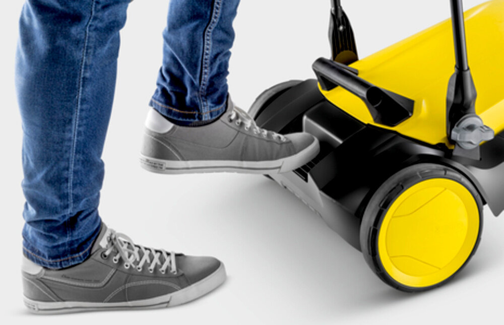 Zamiatarka ręczna KARCHER S4 Twin 2-in-1 1.766-365.0 zbliżenie na uchwyt nożny osoba trzyma stopę na uchwycie uchwyt nożny umożliwia złożenie urządzenia bez schylania się uchwyt transportowy ułatwia przenoszenie