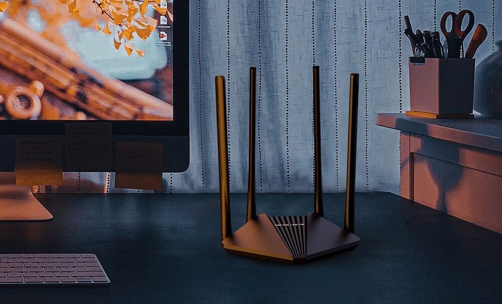 Router MERCUSYS MR30G Router ustawiony na biurku w domowym wnętrzu, obok komputera i przyborów biurowych. Scena jest delikatnie oświetlona, tworząc przytulną atmosferę, testy, odporność, wytrzymałość