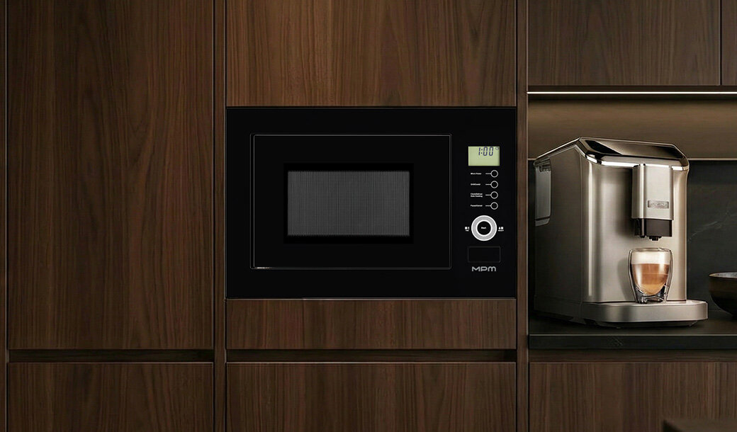 Kuchenka mikrofalowa wbudowana w drewnianą zabudowę kuchenną, z wyświetlaczem pokazującym \'FOO\' i przyciskami po prawej stronie. Obok znajduje się ekspres do kawy z filiżanką kawy na podstawce.