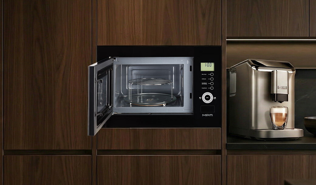 Kuchenka mikrofalowa w zabudowie z otwartymi drzwiczkami, obok ekspres do kawy z filiżanką. Na panelu mikrofalówki widoczny jest wyświetlacz z napisem \'FOd\' oraz logo \'MPM\'.