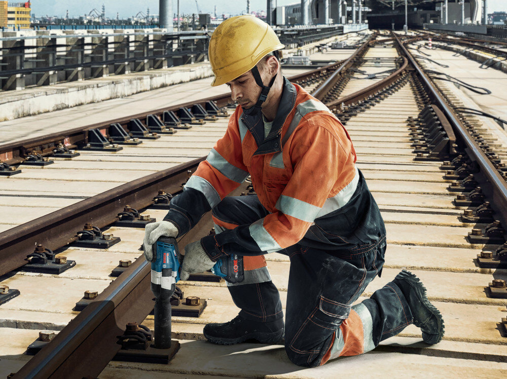 Klucz udarowy BOSCH Professional GDS 18V-1000 06019J8300 tory kolejowe osoba klęczy na torach dokręca śruby przy szynach moc wydajność do ciężkiej pracy