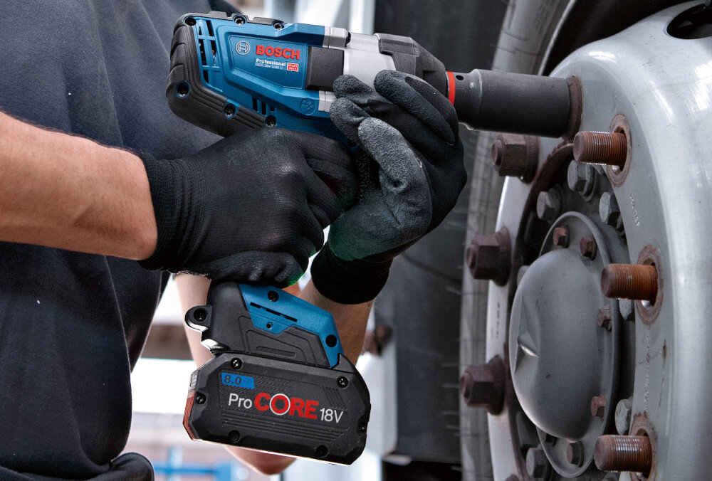 Klucz udarowy BOSCH Professional GDS 18V-1000 06019J8300 warsztat samochodowy osoba dokręca śruby w kole waga około 2,9 kg smukła dobrze wyprofilowana rękojeść pokrycie Softgrip z antypoślizgowego miękkiego materiału długość korpusu wynosząca 240 mm stabilność chwytu ogranicza ślizganie się dłoni