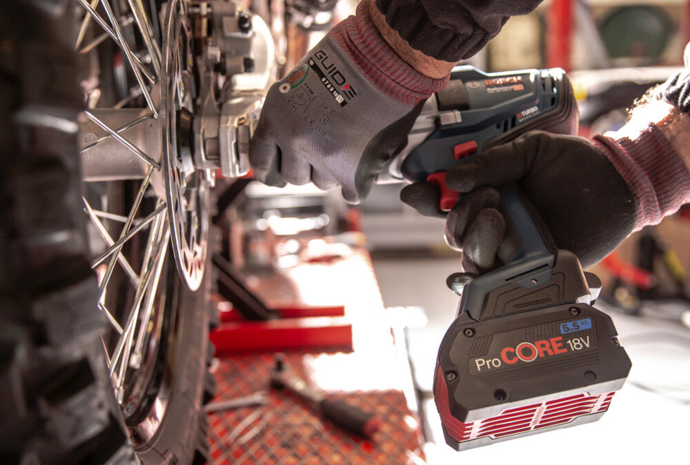 Klucz udarowy BOSCH Professional GDS 18V-1000 06019J8300 warsztat samochodowy osoba dokręca śruby w kole zbliżenie na akumulator współpracuje ze wszystkimi akumulatorami i ładowarkami BOSCH Professional 18 V, ProCORE18V i AMPShare dla wielu marek zaoszczędzisz czas i pieniądze mocne ogniwa ProCORE wyższą wydajność prądową