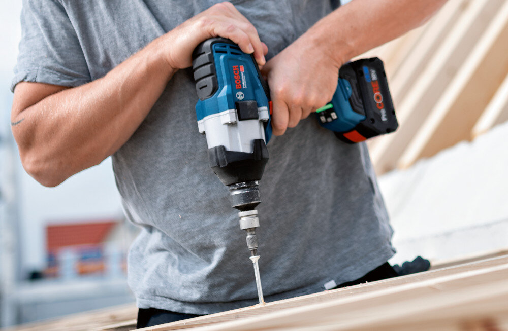 Klucz udarowy BOSCH Professional GDS 18V-1000 06019J8300 pomieszczenie osoba przykręca śrubę do drewnianej belki widoczny wskaźnik wskaźnik statusu gotowości klucza do pracy informacja o poziomie naładowania akumulatora ewentualnych przeciążeniach pozwala szybciej reagować na konieczność ładowania lub przerwę serwisową minimalizuje ryzyko przerwania pracy pełna kontrola nad narzędziem