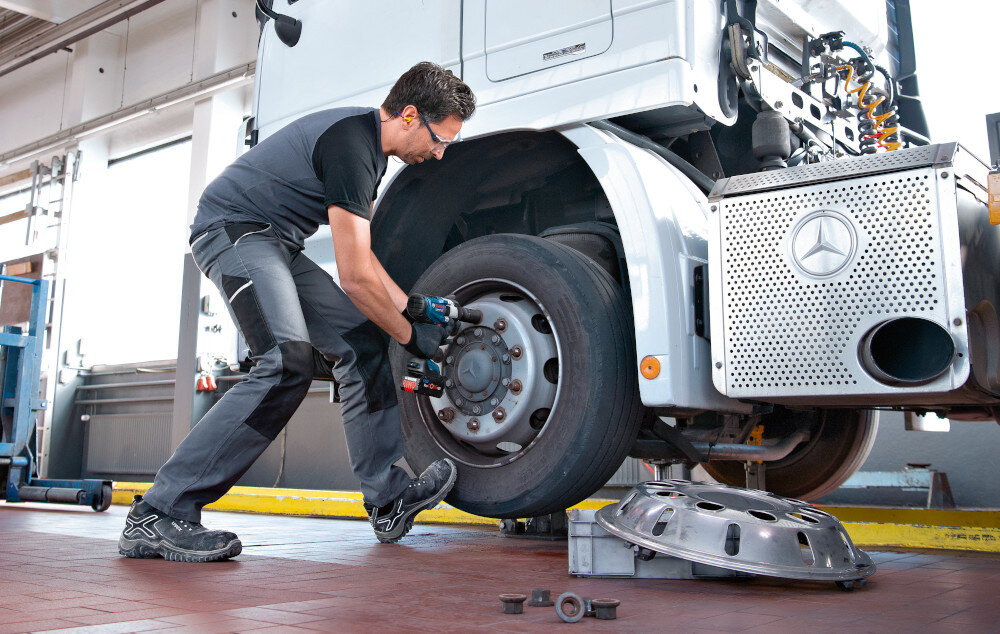 Klucz udarowy BOSCH Professional GDS 18V-1000 06019J8300 warsztat samochodowy osoba przykręca śruby do koła w tle ściana korpus samochodu uchwyt 1/2 cala z pierścieniem osadczym szybkie i bezproblemowe mocowanie nasadek obsługuje śruby w zakresie M10–M24 zwiększa precyzję skraca czas pracy minimalizuje ryzyko uszkodzeń