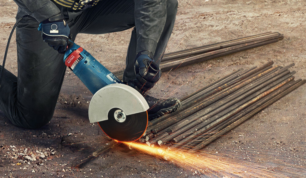 Szlifierka kątowa BOSCH GWS 24-180 P osoba trzyma szlifierkę w dłoniach tnąc metalowe rurki ergonomiczna konstrukcja rękojeści wygodna obsługa ergonomiczna rączka o bardzo małym obwodzie miękka powłoka typu SoftGrip stabilny chwyt