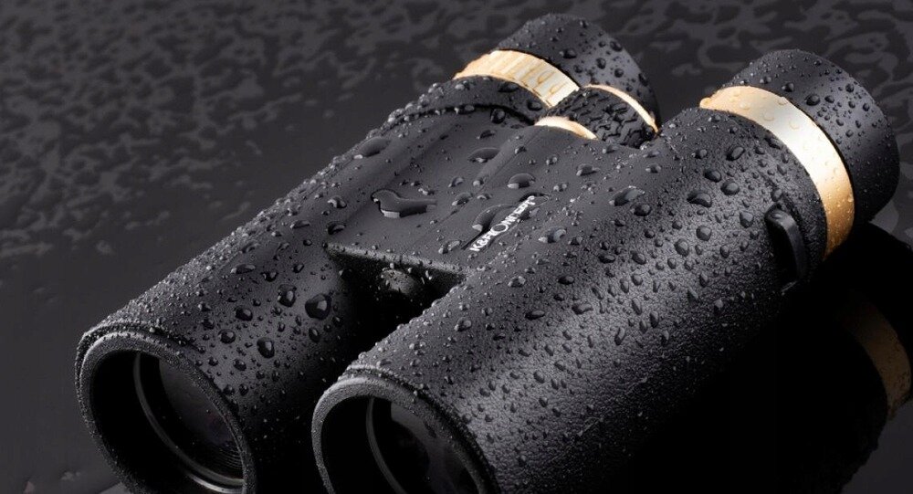 Czarna lornetka pokryta kroplami wody, z widocznym napisem \'K&F CONCEPT\' na obudowie. Lornetka ma złote akcenty na okularach.