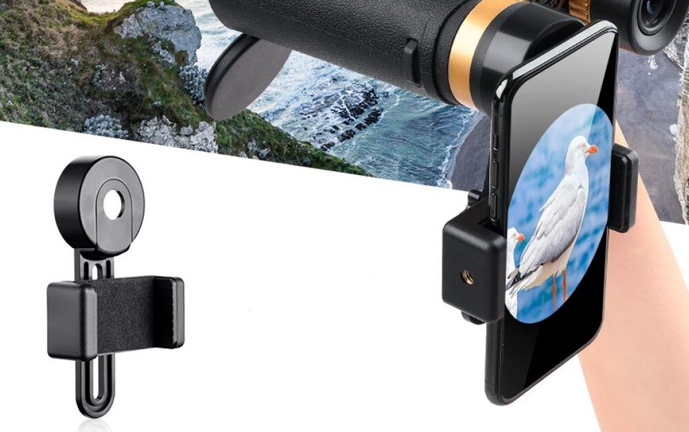 Obraz przedstawia uchwyt do telefonu zamocowany na lornetce, z widocznym ekranem telefonu pokazującym zdjęcie mewy. W tle widać fragment krajobrazu z klifem i morzem.