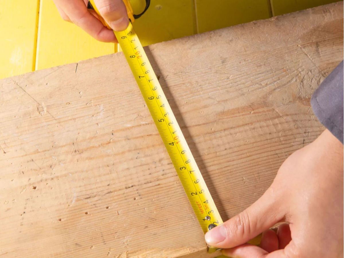 Miara zwijana DELI TOOLS EDL9005Y (5 m), precyzyjne, oznaczenia, milimetry, cale, osoba odmierza przy pomocy miary szerokość deski