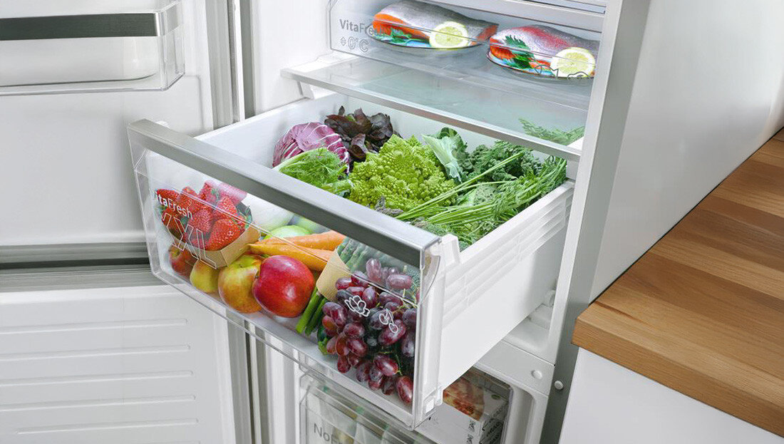 LODÓWKA BOSCH KGN39LBCF BLACK Zdjęcie przedstawia wysuniętą szufladę lodówki z pojemnikiem wypełnionym świeżymi warzywami i owocami, takimi jak sałata, winogrona czy jabłka. W tle widać górne półki chłodziarki z zapakowanymi produktami strefa VitaFresh XXL szuflada dużo miejsca regulacja wilgotności warzywa owoce ryby mięso