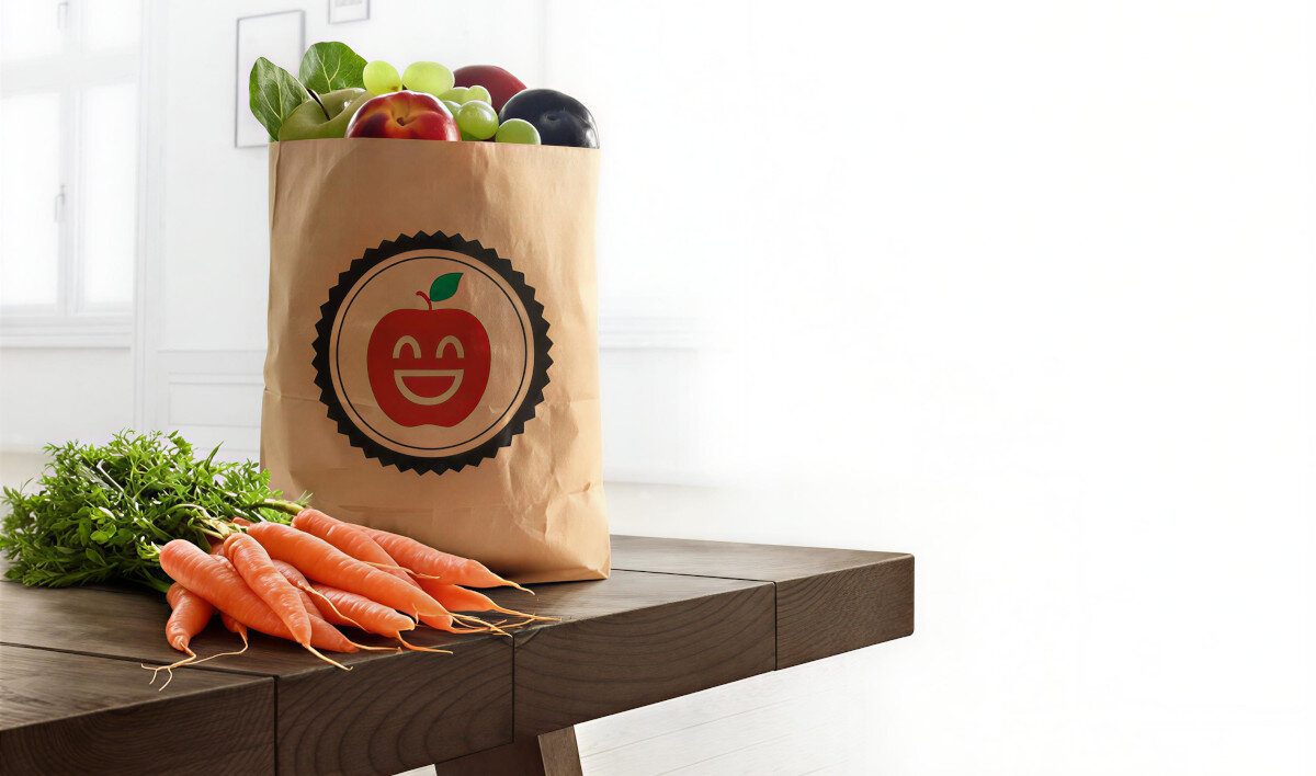 LODÓWKA BOSCH KGN39LBCF BLACK Zdjęcie przedstawia papierową torbę wypełnioną świeżymi owocami i warzywami, stojącą na drewnianym stole obok pęczka marchewek. Na torbie znajduje się graficzne logo z uśmiechniętym jabłkiem szybkie chłodzenie Superchłodzenie niska temperatura
