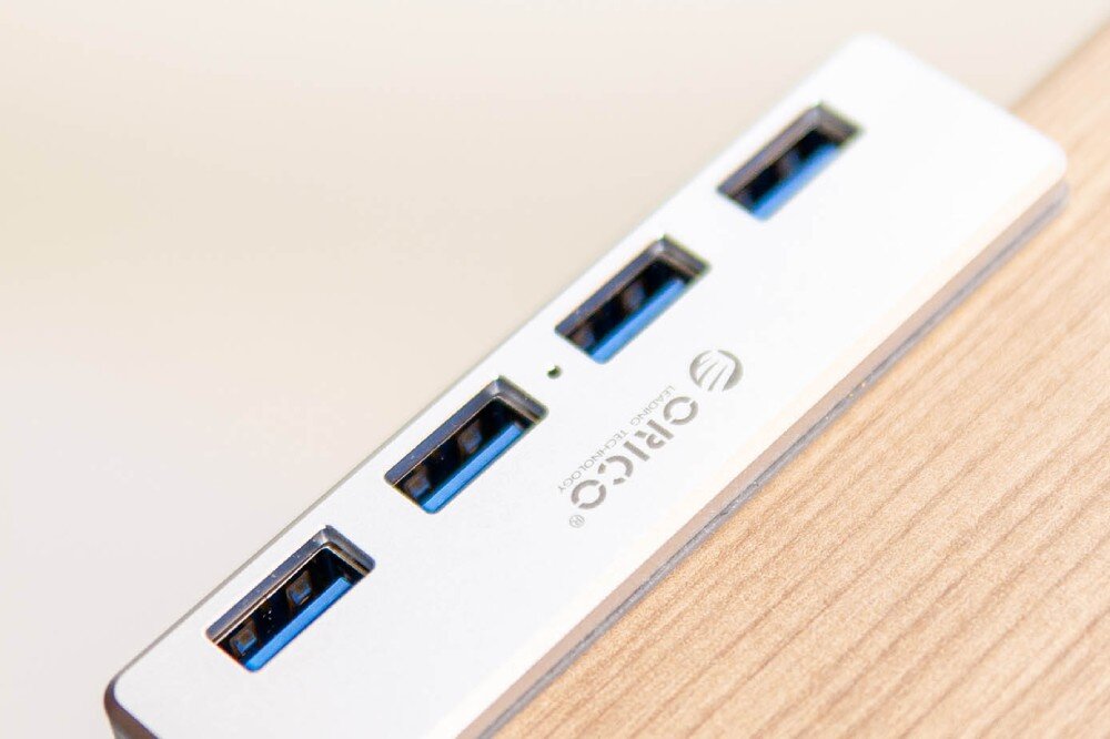 Hub ORICO MH4PU-P-SV-BP Srebrny hub USB z czterema portami zamontowany na brzegu drewnianego biurka, gniazda, prędkość, przepustowość