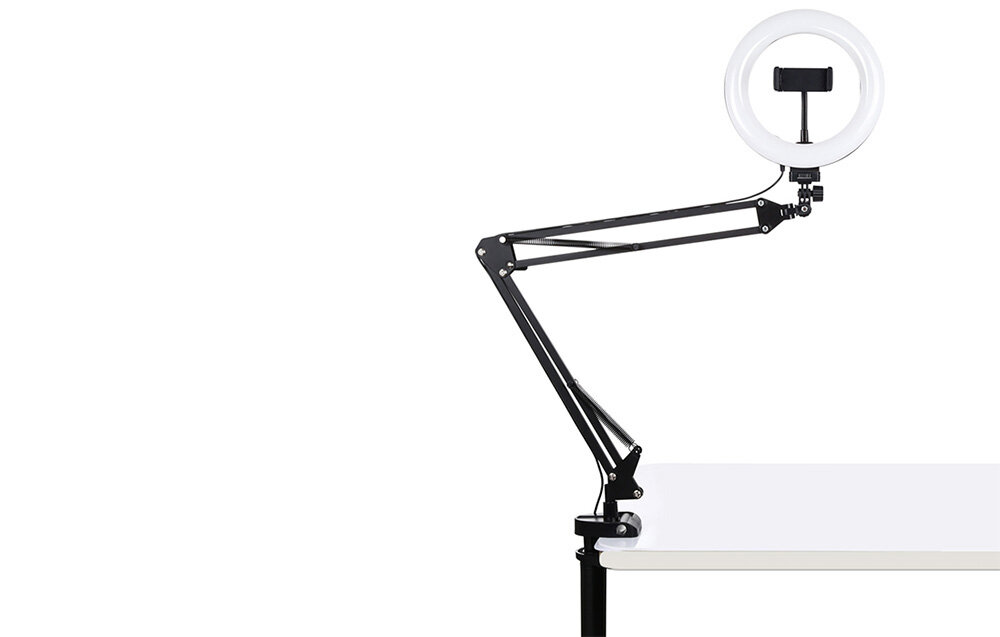 Lampa pierścieniowa LED zamontowana na regulowanym ramieniu przymocowanym do blatu stołu. Lampa posiada uchwyt na smartfon w środku pierścienia.