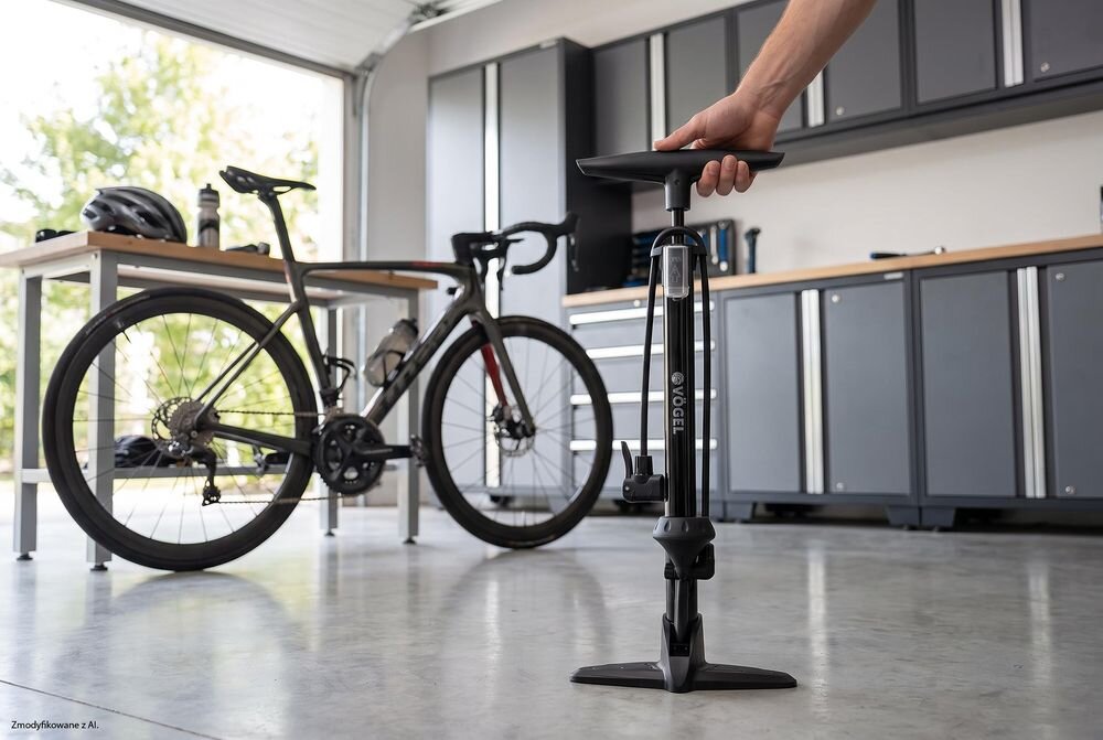 Na zdjęciu widoczna jest część roweru z pompką rowerową o pomarańczowym kolorze. Na pompce znajduje się przezroczysta osłona z napisem \'OPEN\'.