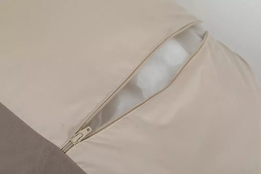 Legowisko dla kota ZOLUX Chambord ze zdejmowaną poszewką do prania w 30 stopniach Zbliżenie na róg legowiska, pokazujące rozpięty zamek błyskawiczny. Widoczny beżowy materiał pokrowca i białe wypełnienie w środku, co sugeruje możliwość prania poszewki.