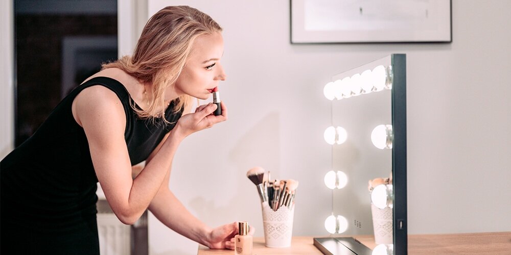 Kobieta w czarnej sukience nakłada szminkę przy prostokątnym lustrze Humanas z podświetlanymi lampkami
